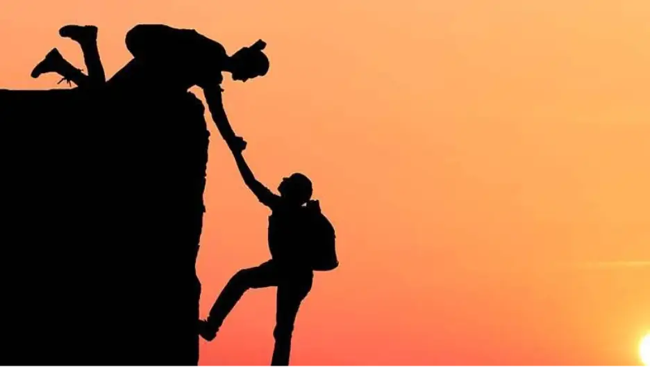 One climber reaches down to help another up a steep mountain face
